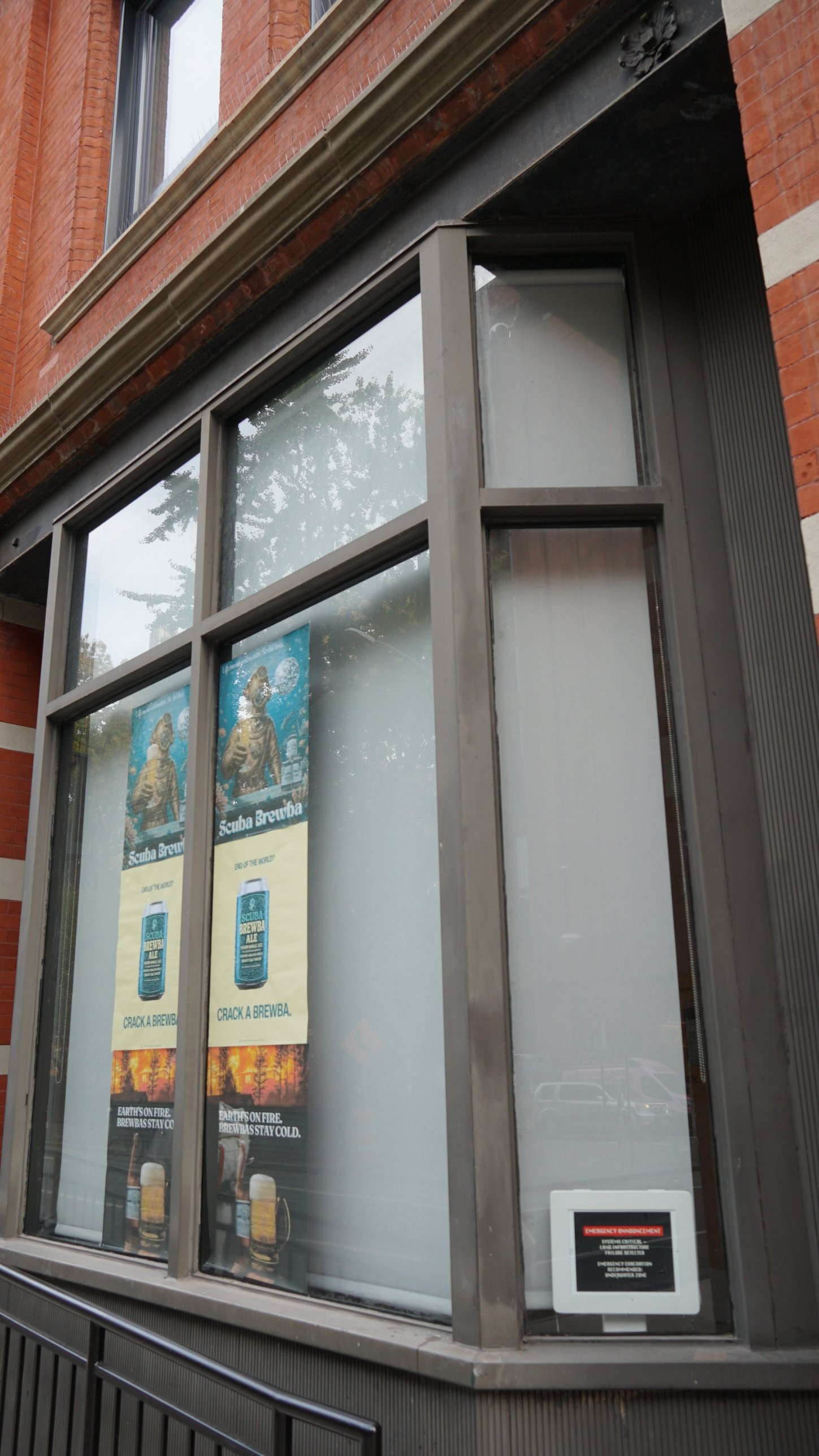 Looking up at the gallery window: Scuba Brewba posters and the emergency announcement screen